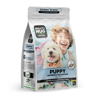 A packaging bag of Puppy, Nutrients for Growth Formula Dog Food for Medium & Large Breeds Nature's Hug, emphasizing nutrient growth for the first year. The front of the bag showcases a joyful child laughing while holding a fluffy white puppy. Text highlights the product’s features, including "Sustainable Complete Protein" and "Complete and Balanced Food for Puppies." The vibrant colors and playful design appeal to pet owners.